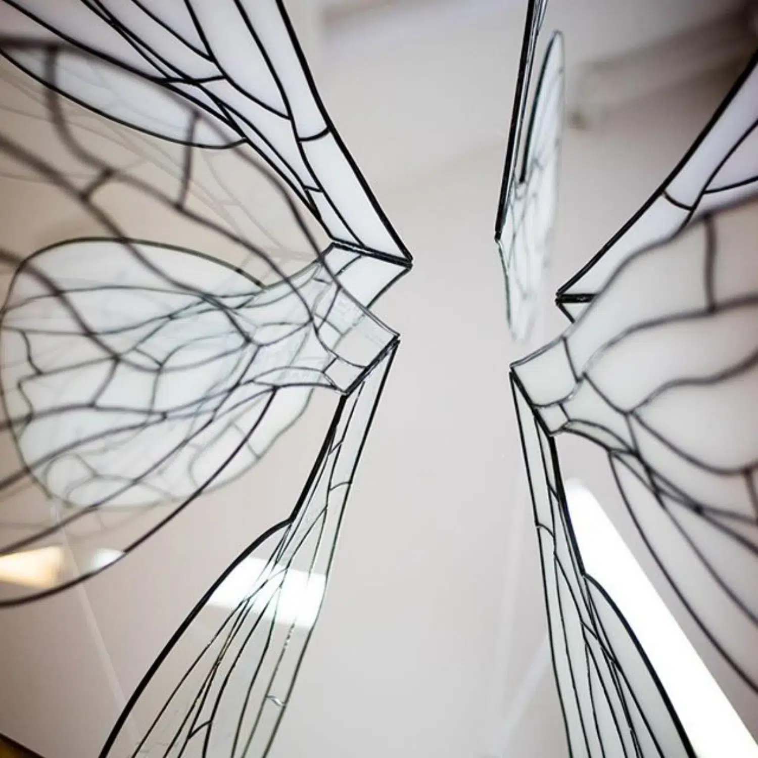 Gros plan de l'installation d'ailes en vitrail déposées verticalement et en cercle sur un miroir.