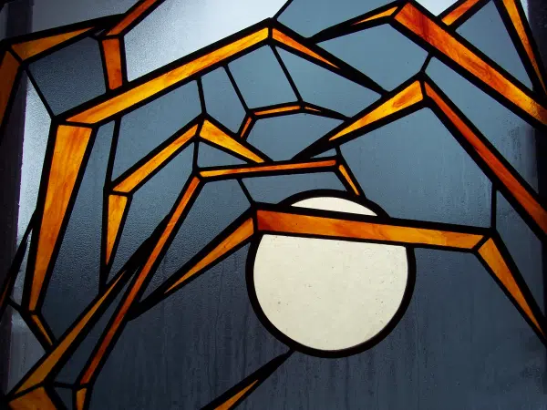 Détail d'un vitrail rond avec des motifs de pattes d'insecte en verre orangé sur un fond gris.